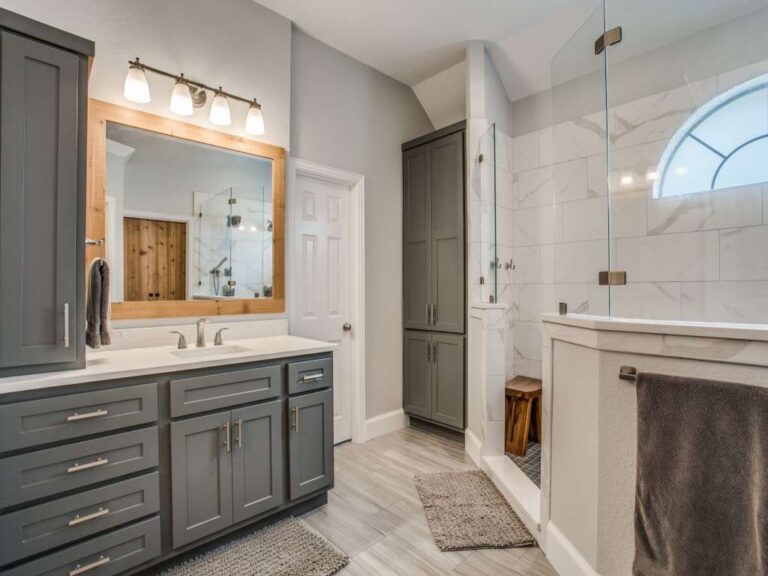 a-modern-bathroom-interior-features-gray-cabinets-and-drawers-a-large-framed-mirror-and-bright-vanity-lightning-above-the-sink