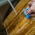 a-person-cleaning-a-wooden-cutting-board-with-a-blue-sponge