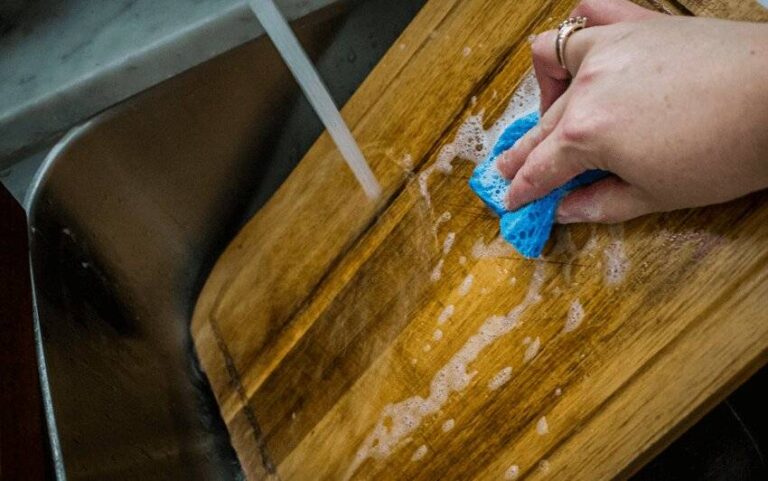 a-person-cleaning-a-wooden-cutting-board-with-a-blue-sponge