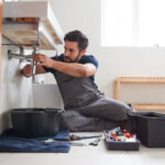 a-professional-male-plumber-sitting-on-the-floor-to-repair-plumbing-underneath-a-sink