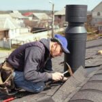 a-roofer-working-on-an-asphalt-shingle-roof-next-to-a-modern-black-modular-metal-chimney
