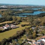 a-several-rows-of-new-build-houses-with-distinctive-roofs-set-within-a-lush-green-landscape