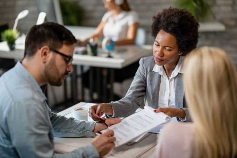 Smart Strategies For Building A Vacation Rental Portfolio a-woman-holding-a-pen-sitting-behind-a-desk-and-actively-speaking-to-or-advising-her-clients