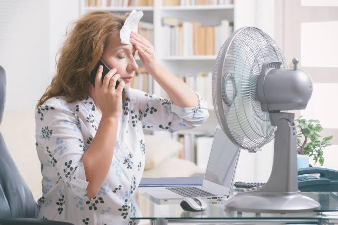 How Hot is Too Hot to be Without an AC Unity in Your Home a-woman-is-holding-a-wet-wipe-or-cool-cloth-against-her-forehead-and-sitting-directly-in-front-of-running-fan