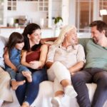 the-three-generations-a-grandparents-in-the-center-their-adult-children-and-their-two-young-kids-they-are-gathered-in-a-modern-living-room