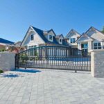 a-large-black-wrought-iron-driveway-gate-featuring-a-prominent-arched-top-rail-the-gate-is-framed-by-two-substantial