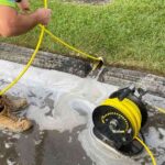 a-plumber-is-feeding-a-high-pressure-line-into-an-outdoor-drain-opening-situated-along-the-edge-of-a-green-lawn-and-concrete-surface