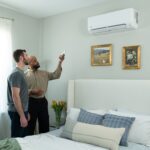 an-indoor-scene-in-a-brightly-lit-modern-bedroom-with-light-colored-walls-a-man-is-guiding-other-man-about-split-air-conditioner