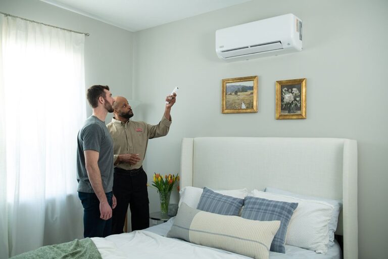 Ductless Mini-Splits Explained: A Homeowner’s Guide to Room-by-Room Comfort an-indoor-scene-in-a-brightly-lit-modern-bedroom-with-light-colored-walls-a-man-is-guiding-other-man-about-split-air-conditioner