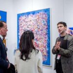 three-individuals-are-standing-inside-a-modern-well-lit-art-gallery-space-they-are-actively-gesturing-with-his-hands-as-explaining-a-art