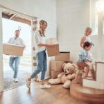 an-indoor-residential-entryway-featuring-a-man-and-woman-holding-a-cardboard-box-and-children-is-walking-up-stairs