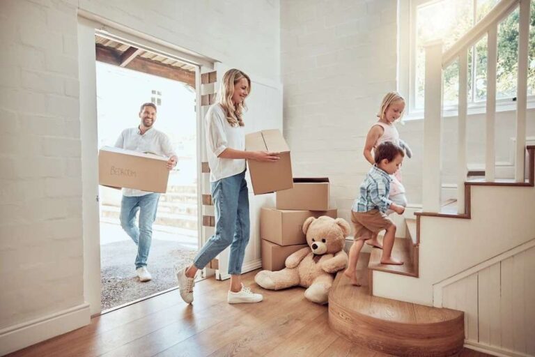 A Guide To Moving Homes In 2026 an-indoor-residential-entryway-featuring-a-man-and-woman-holding-a-cardboard-box-and-children-is-walking-up-stairs