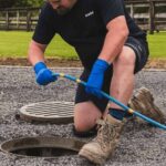 the-individual-is-manually-feeding-or-pulling-a-long-blue-flexible-rod-or-plumbing-snake-directly-into-the-open-drain