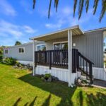 a-single-story-mobile-or-manufactured-home-featuring-tan-exterior-siding-dark-trim-and-a-prominent-front-porch-structure